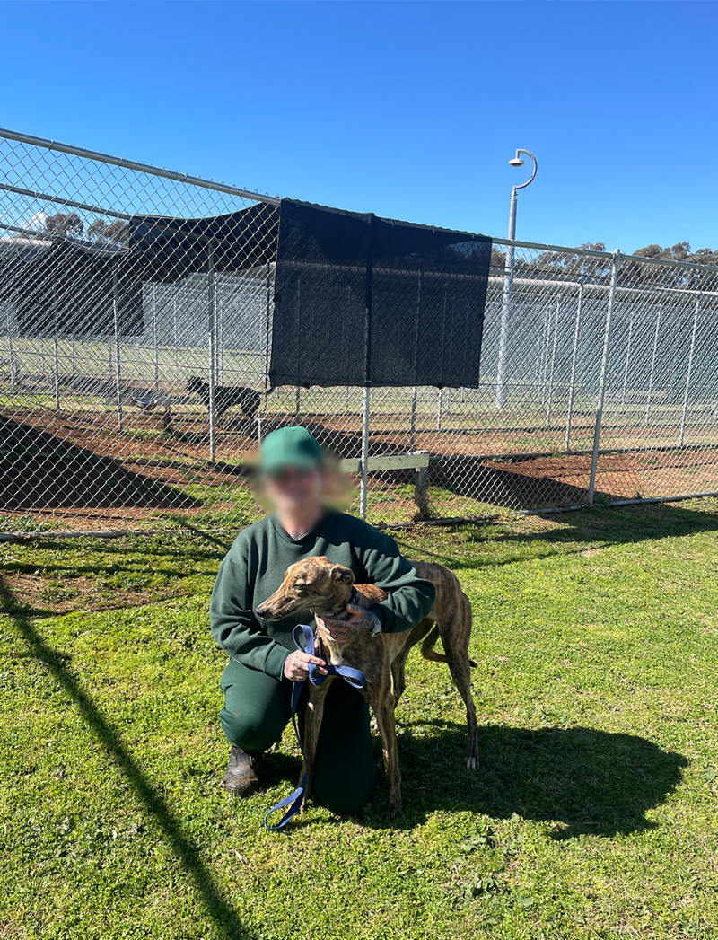 Inmate in green tracksuit, kneeling with one arm around greyhound.