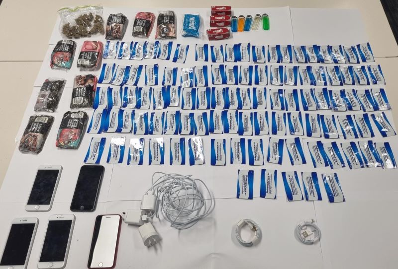 A table laid in rows, with 5 phones, 3 mobile phone charges, 2 usb cables, scores of buprenorphine strips, 10 packets of tobaccor, cigarette filters, five lighters.