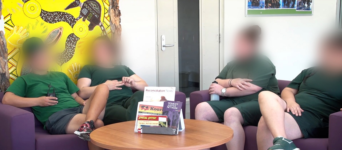 Four women seated in armchairs in front of an bright yellow indigenous artwork, wearing green tshirts and shorts, and sneakers.