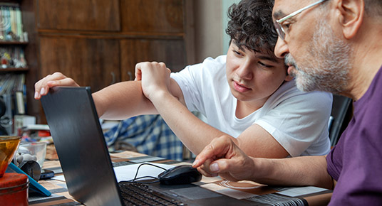 Grandson is Pointing to his Grandfather at Laptop Monitor