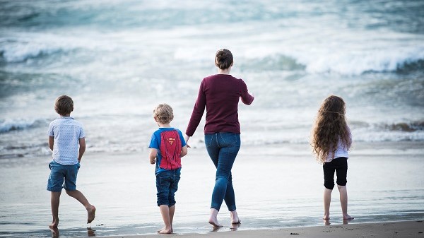 Ella walking with her three children towards the water at the beach. Their back is towards the camera. 