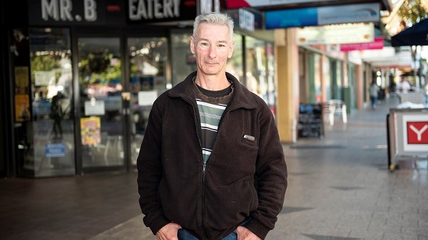Garry smiling at the camera while he stands in front of local stores.