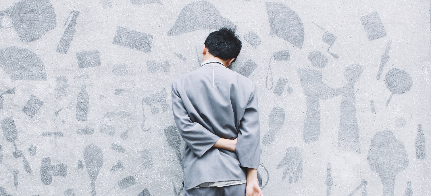Man with hands behind back facing a wall