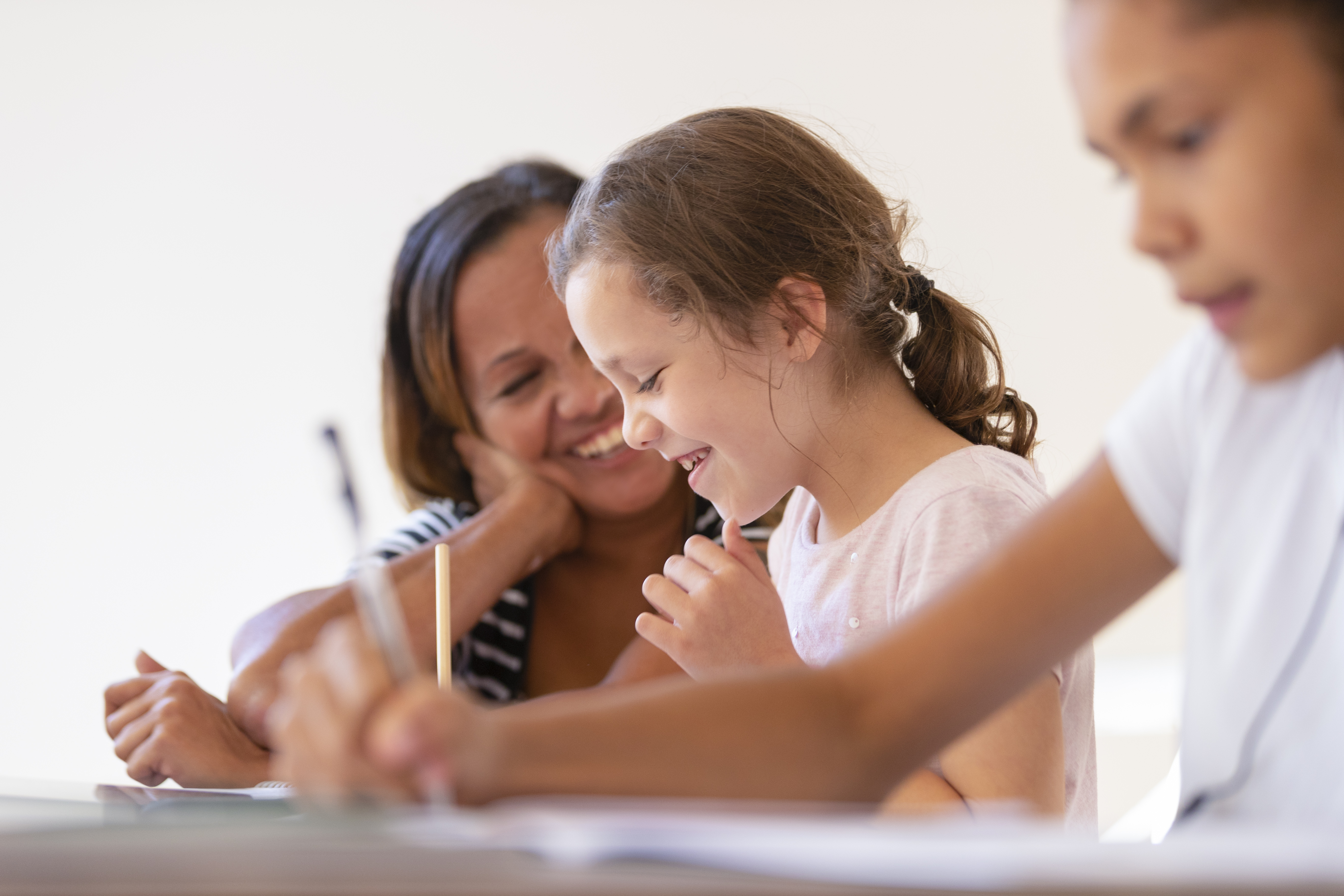 A mother smiling at two children sitting at a desk writing