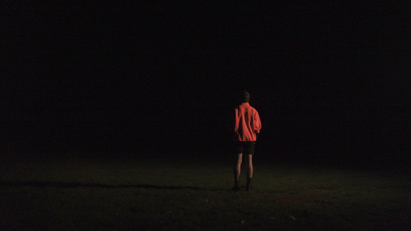 An image of a young man near an outside fire, in the shadows